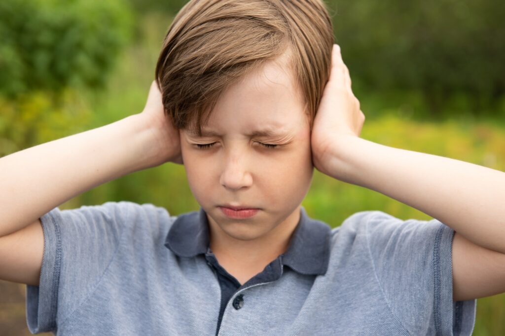 Little Caucasian boy closing ears with his hands. Childhood traumatic experience, psychology